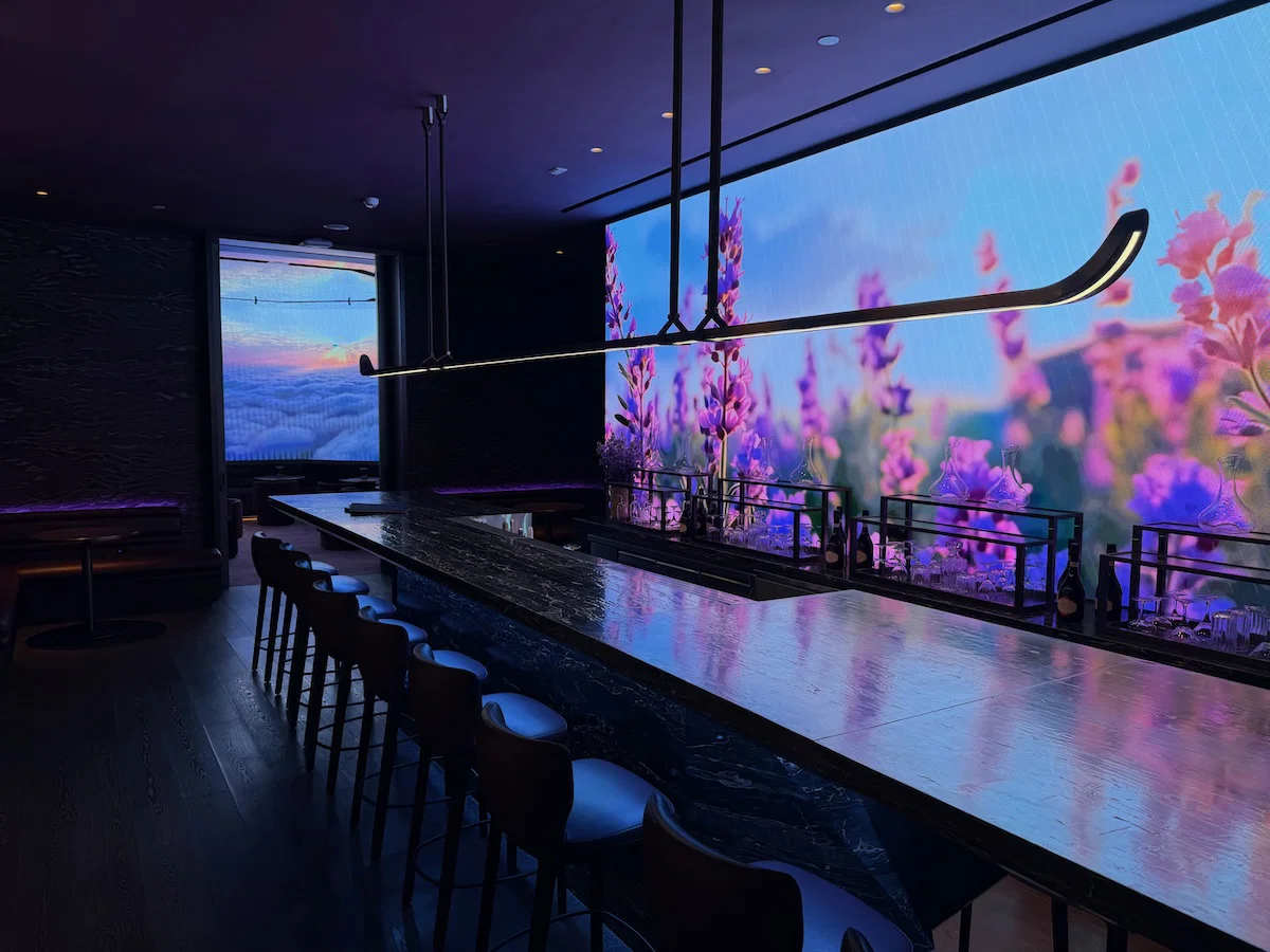 Interior of a premium airport lounge bar with dark marble counter, high stools and immersive digital wall display